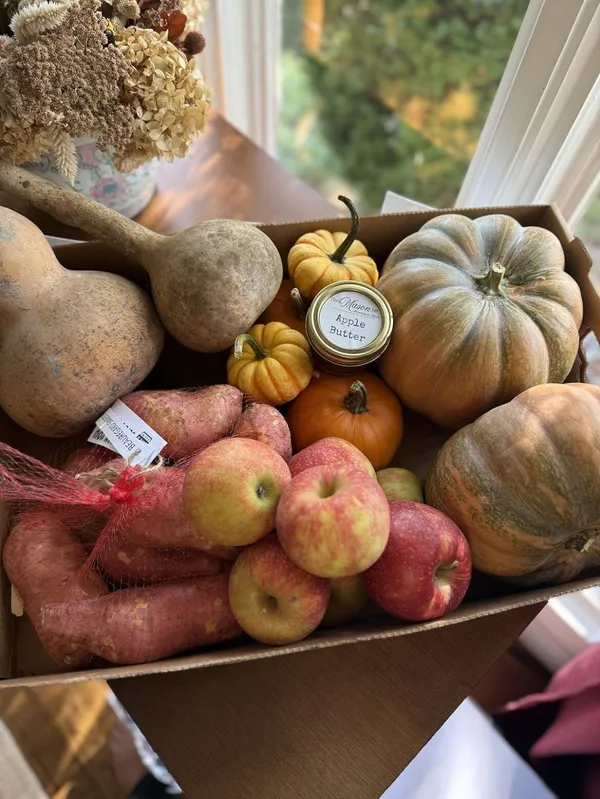 Box of seasonal local produce including squash, apples, and apple butter